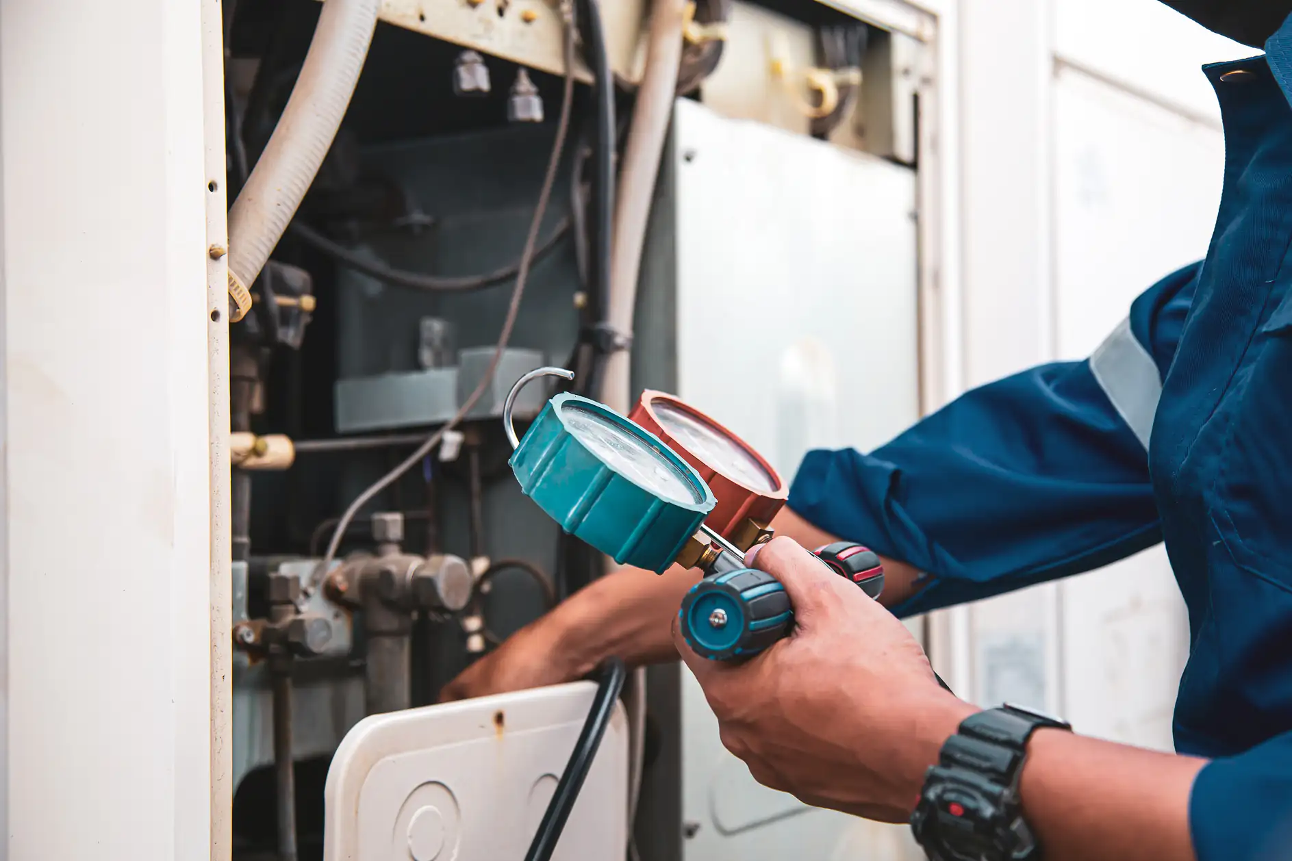 A technician in a blue uniform checks and adjusts gauges on HVAC equipment in TX, using tools to measure pressure and maintain the system for ac replacement Bexar County.